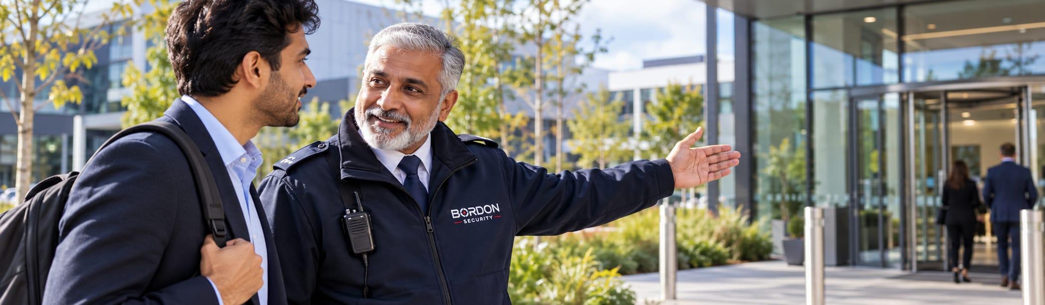 A Bordon Security officer points a visitor towards an office building entrance across a landscaped business campus.